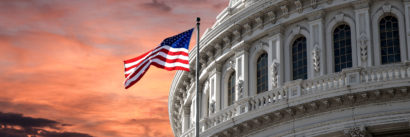 A view of the US capitol during sunset with a flag in the foreground.