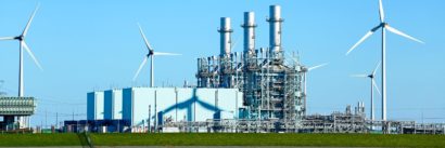 A view of a power plant with wind mills surrounding it.